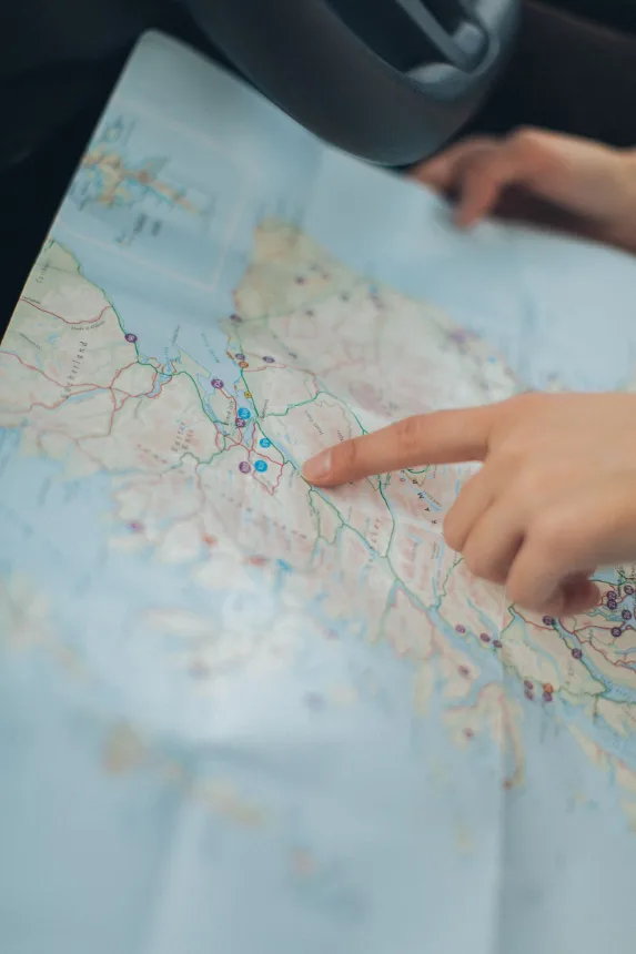 Mao apontando um destino sobre um mapa aberto durante o planejamento da viagem